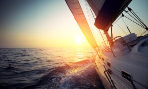 sail boat gliding on open sea at sunset